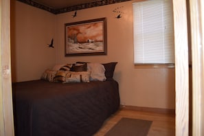 Ein Schlafzimmer mit einem Bett, einem Bild an der Wand und einem Fenster mit Jalousien.