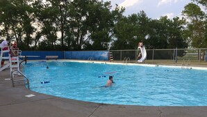 Una piscina con tablado de salto, una silla de salvavidas y zona delimitada por una valla.