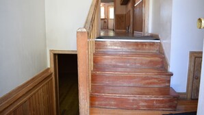 Una escalera de madera con barandilla que lleva a un espacio interior con paredes de madera y una puerta en la parte superior.