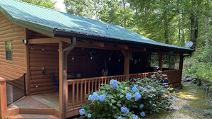 Eine Holzhütte mit Veranda, umgeben von einem Kiesweg und blau blühenden Hortensienbüschen.