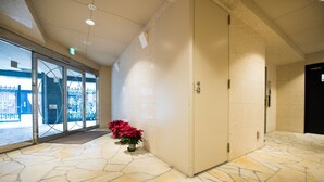 A lobby with a stone floor, a reception desk, and a potted plant with red flowers. - Very Hotel Dotonbori (Osaka)