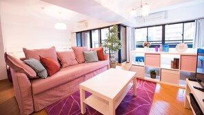 A modern living room with a pink sofa, a white coffee table, and a large window with a view of buildings. - Very Hotel Dotonbori (Osaka)