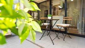 A patio area with a table and two chairs, a potted plant, and a view through a glass door. - Very Hotel Dotonbori (Osaka)