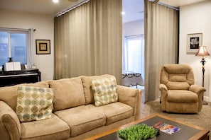 Una sala de estar con un sofá color crema, un sillón a juego, una mesa de centro con una planta y un piano al fondo.
