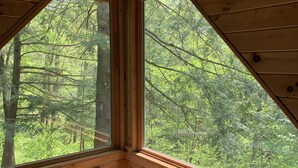 Una habitación con techo de madera, una cama con colcha blanca y amplios ventanales con vistas a un bosque.