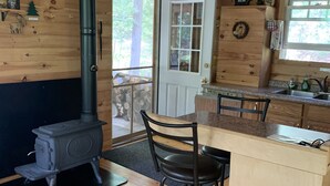 Acogedor interior de cabaña con estufa de leña, comedor con banco y cocina con pileta y mostrador.
