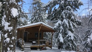 Una cabaña de madera con un porche, rodeada de árboles cubiertos de nieve.