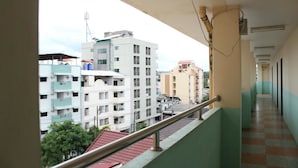 Un pasillo con barandilla metálica que conduce a un balcón con vistas a edificios de varios pisos.