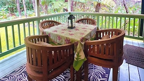 Un espace extérieur aménagé, abrité et doté d’une table et de chaises, entouré d’une terrasse en bois et d’une végétation luxuriante.