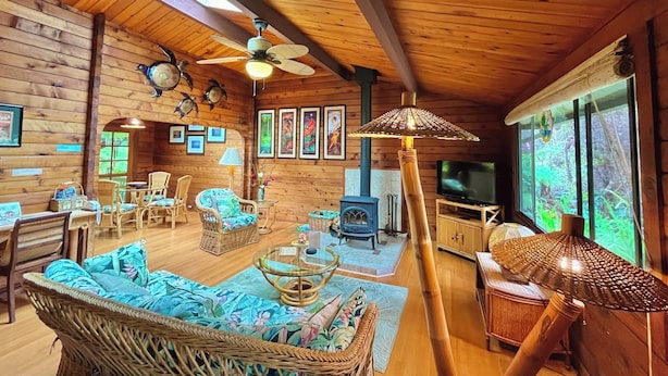 L’intérieur d’un chalet en bois chaleureux et accueillant, avec un coin repas, des sièges, une cheminée et une grande fenêtre.