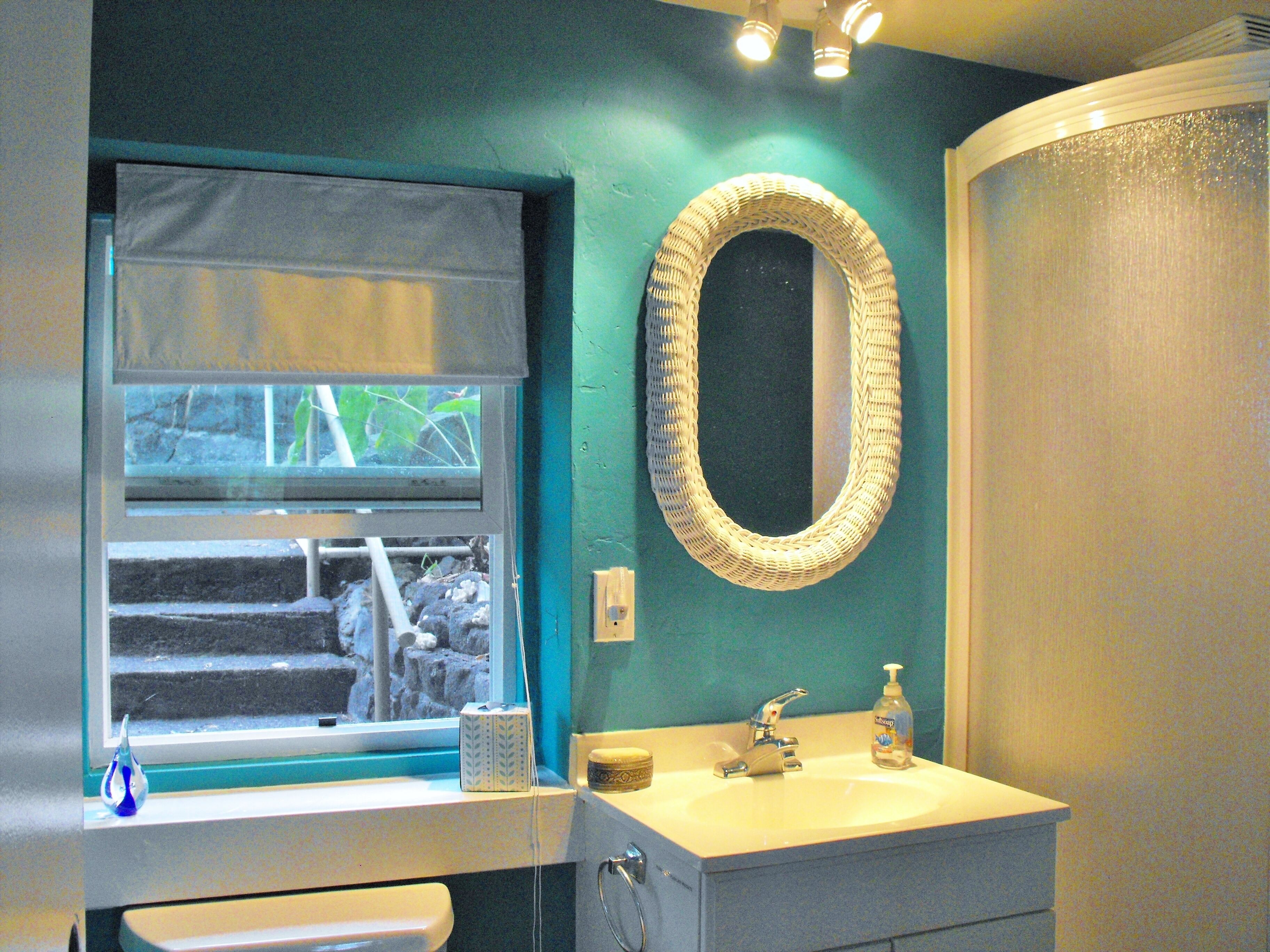 A bathroom with a window, a sink, a mirror, and a shower area.