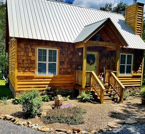 Une cabane en bois avec un toit en métal, une véranda dotée d’une balustrade en bois et des fondations en pierre.