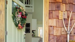 Une porte en bois ornée d’une guirlande, un pot en céramique blanche et un mur en bois.