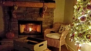 Un salon chaleureux avec une cheminée, un fauteuil en osier et un sapin de Noël.