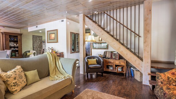 A cozy living room with a wooden staircase, a sofa, a chair, and a small table with books and decorative items. - Villa Pine Mountain- country cottage get away (green) Central AC  (Pine Mountain Club)