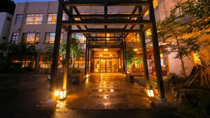 A building entrance with a wooden archway, a wet ground, and potted plants. - Hosenji Kanko Hotel Yumotoya (Kokonoe)