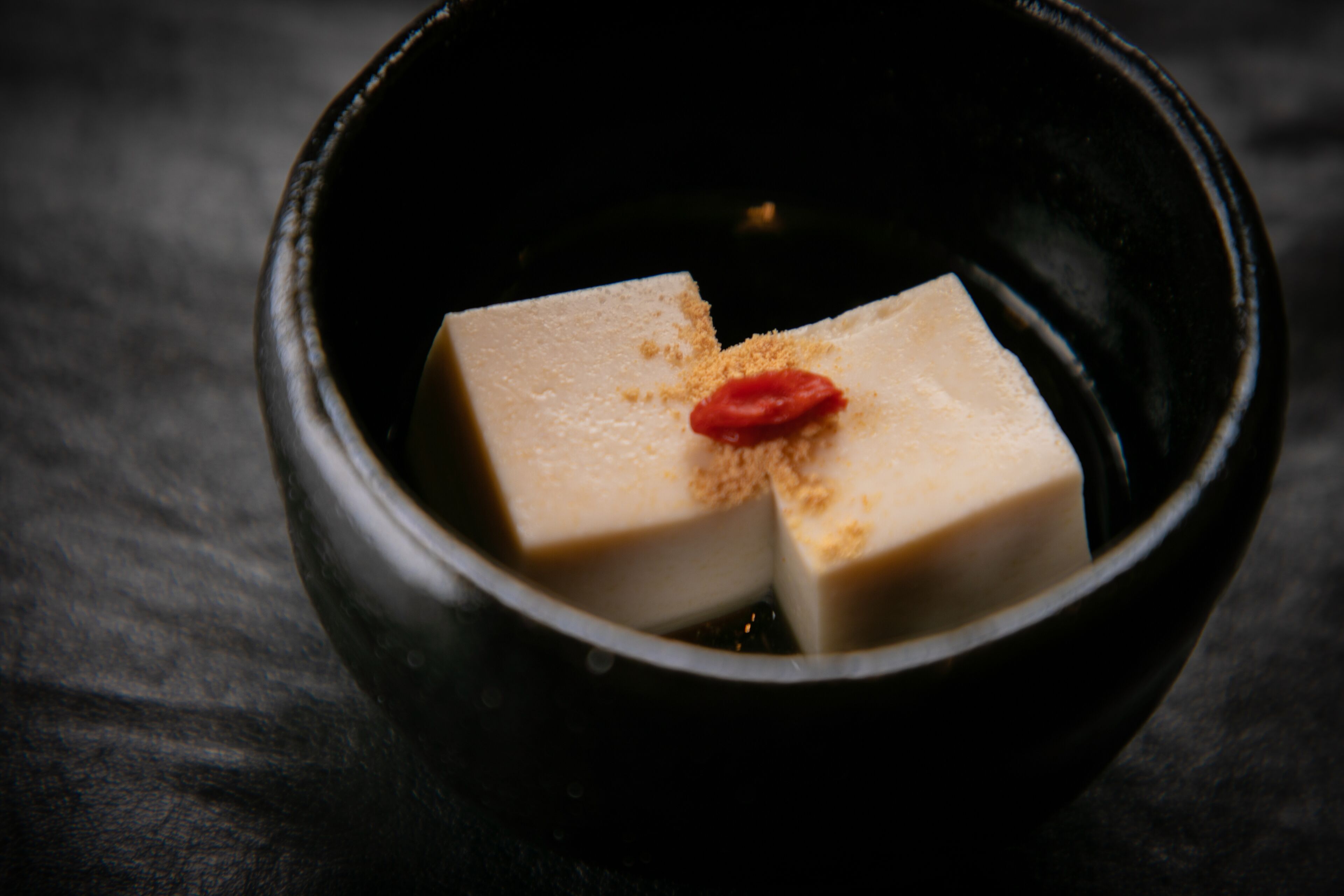 A black bowl containing a white cube with a red dot and a brown powder.