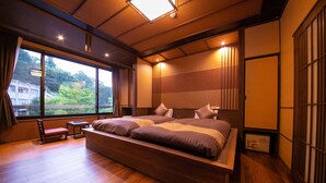 A modern hotel room with a large bed, wooden flooring, a view of greenery outside, and traditional Japanese sliding doors. - Hosenji Kanko Hotel Yumotoya (Kokonoe)