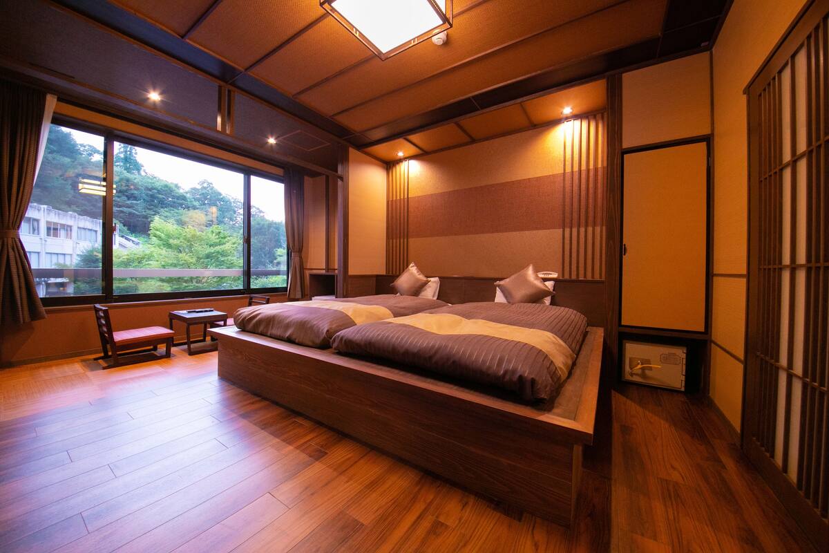 A modern hotel room with a large bed, wooden flooring, a view of greenery outside, and traditional Japanese sliding doors.
