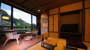 A modern living room with a large TV, wooden furniture, and a view of greenery outside. - Hosenji Kanko Hotel Yumotoya (Kokonoe)