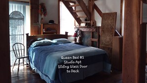 A studio apartment with a queen bed, a ceiling fan, a sliding glass door to the deck, and wooden beams. - River View. Rent Historic Mill's 2nd Floor. Rustic Timber-frame Construction (Shell Rock)
