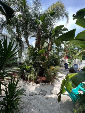 A tropical garden with various plants and a seating area with chairs.
