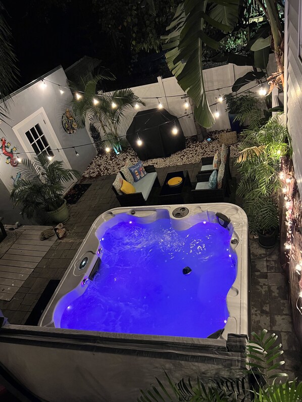 A hot tub with a blue light, surrounded by outdoor furniture and plants.