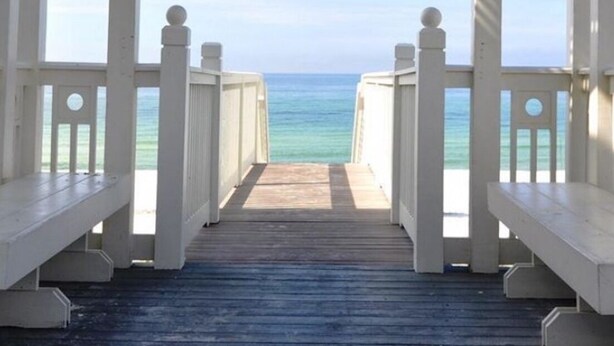 A wooden deck leading to a beach with a clear view of the ocean.