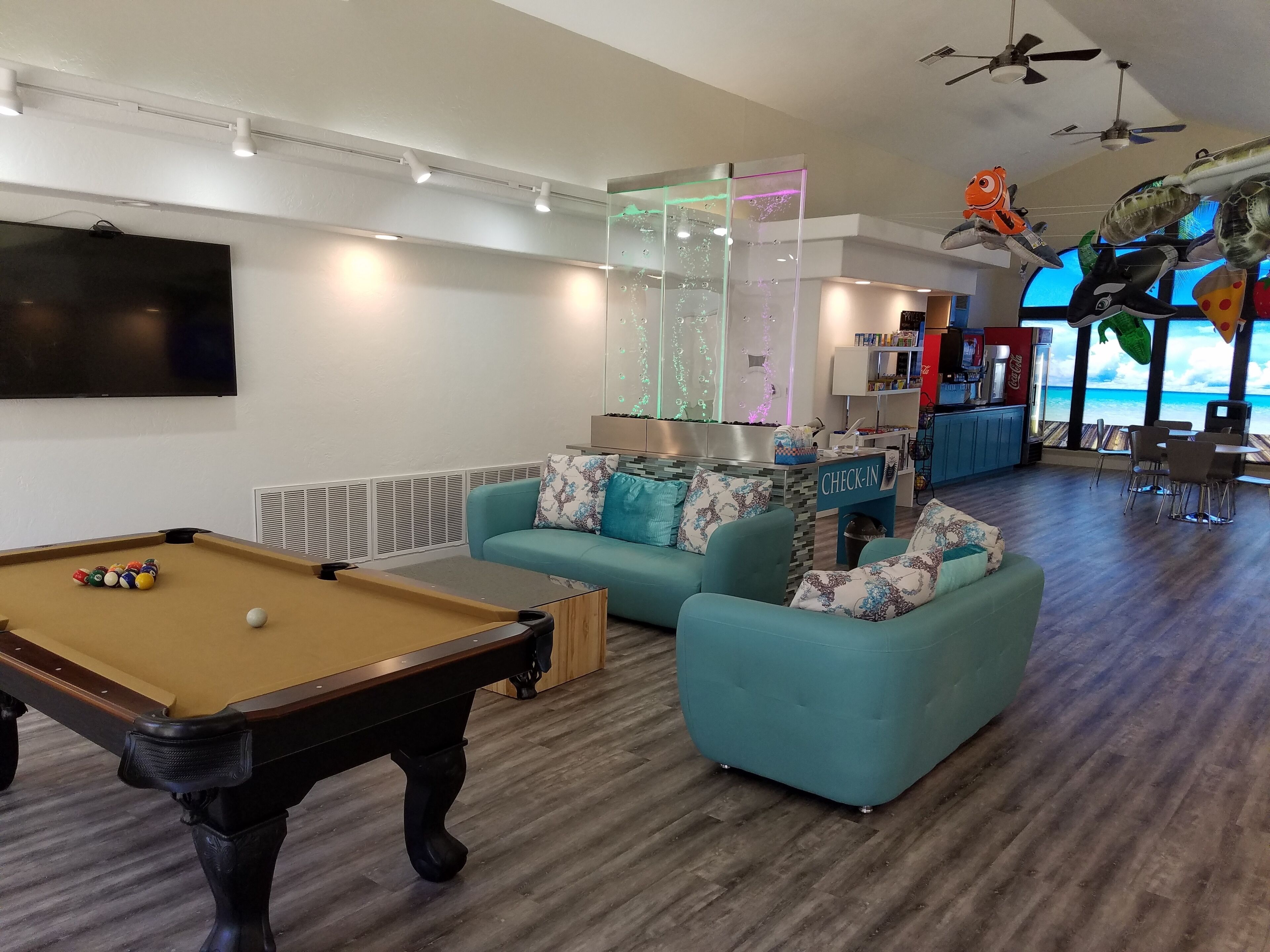 Een moderne woonkamer met een pooltafel, blauwgroene banken, een receptiebalie en uitzicht op de oceaan.