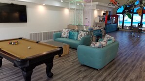 A modern living room with a pool table, teal sofas, a check-in counter, and a view of the ocean. - Comfortable condo close to mountain biking, swimming pools, national parks (St. George)