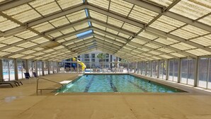 An indoor swimming pool with clear glass walls, a pool ladder, and a slide. - Comfortable condo close to mountain biking, swimming pools, national parks (St. George)