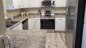 A modern kitchen with white cabinets, stainless steel appliances, granite countertops, and a dishwasher. - Comfortable condo close to mountain biking, swimming pools, national parks (St. George)