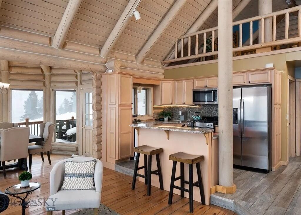 A log cabin interior with a kitchen, dining area, and a balcony.