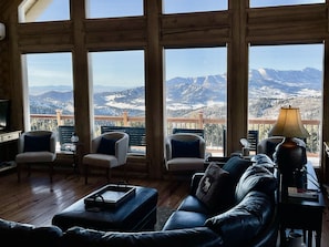 A cozy living room with a large window offering a mountain view. There are two armchairs, a sofa, and a coffee table.