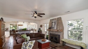 A spacious living room with a fireplace, a large window, and a kitchen in the background.