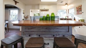 A kitchen with a wooden island, bar stools, and green glass jars.