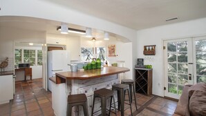 A kitchen with a wooden island, bar stools, a wine rack, and a view through the glass door.
