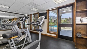 Una palestra con tapis roulant, vista sulla piscina e uno scaffale in legno con asciugamani.