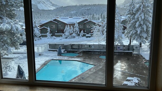 Vista di una casa con piscina, circondata da alberi e montagne innevate.