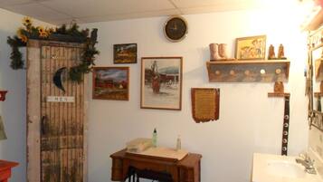 Un baño rústico con puerta de madera, una máquina de coser antigua, un reloj y diversas decoraciones en la pared.
