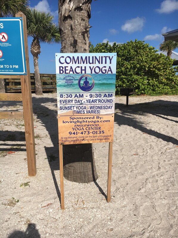 A beach yoga sign with details about the event, including time and contact information.