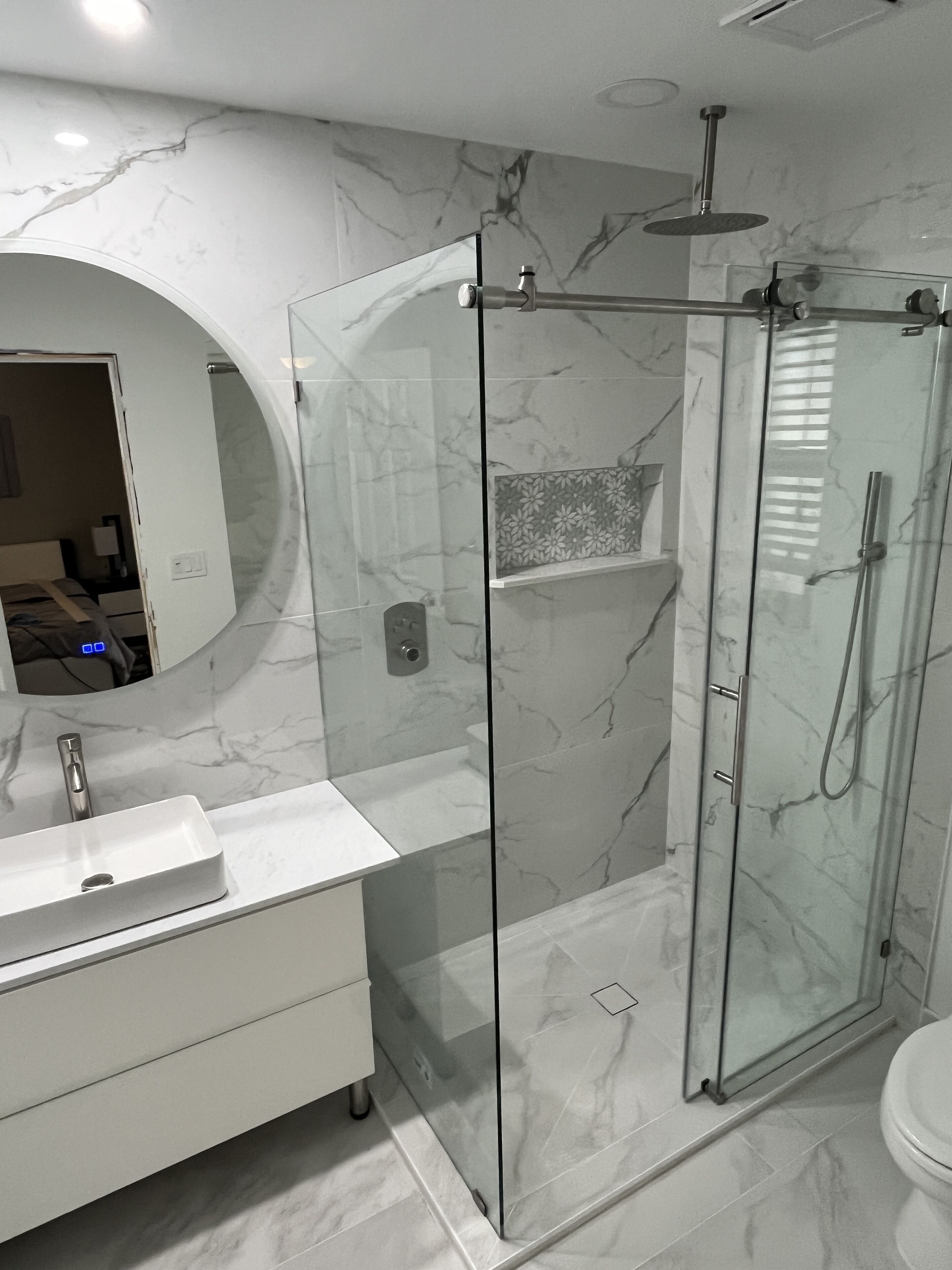 Een moderne badkamer met een douchecabine van glas, een witte wastafel en een vloer van marmer.