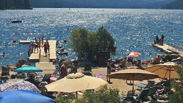 Vista de un lago con muelle, personas y montañas al fondo.