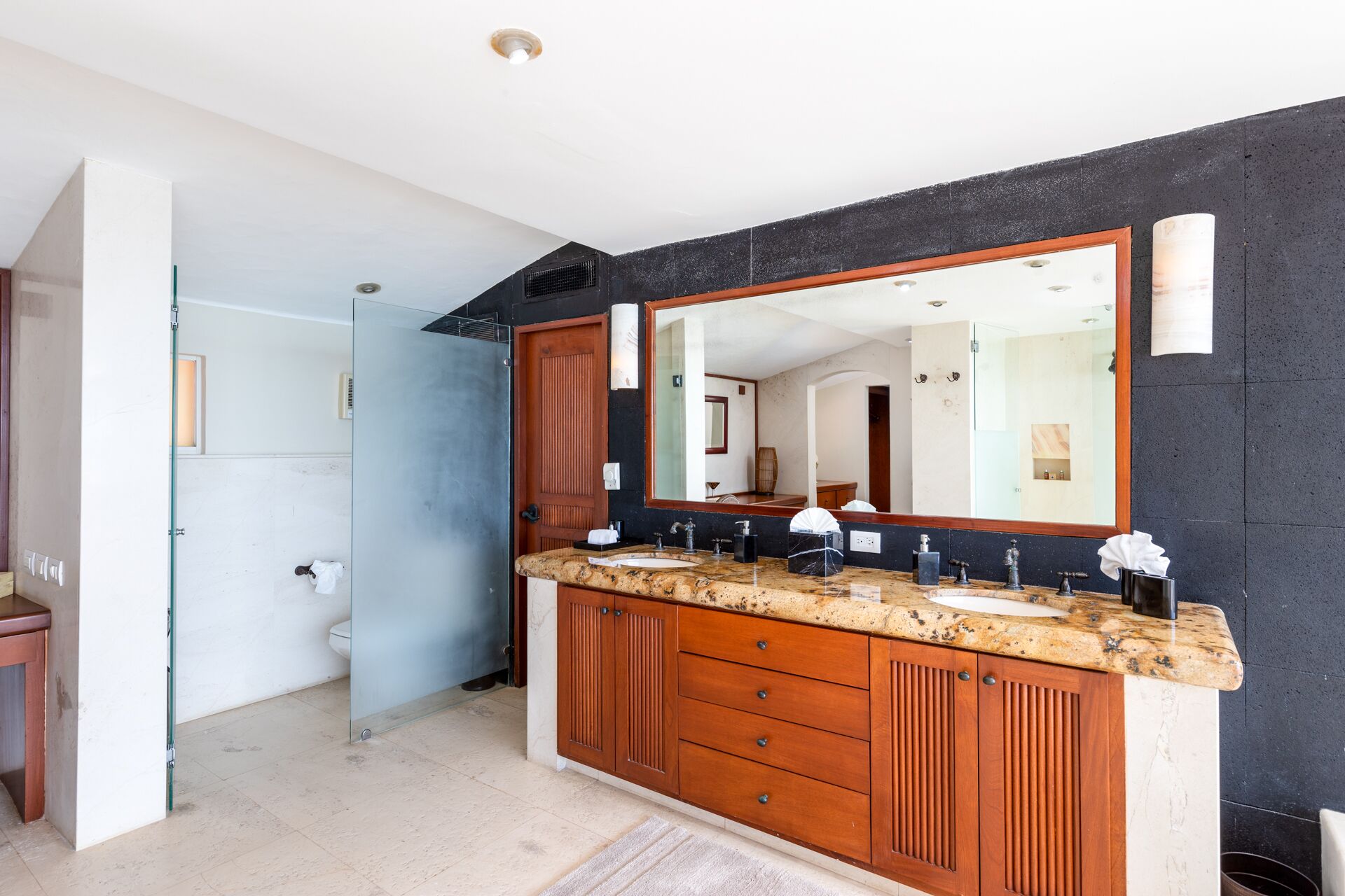 A modern bathroom with a large mirror, wooden cabinetry, and a granite countertop.