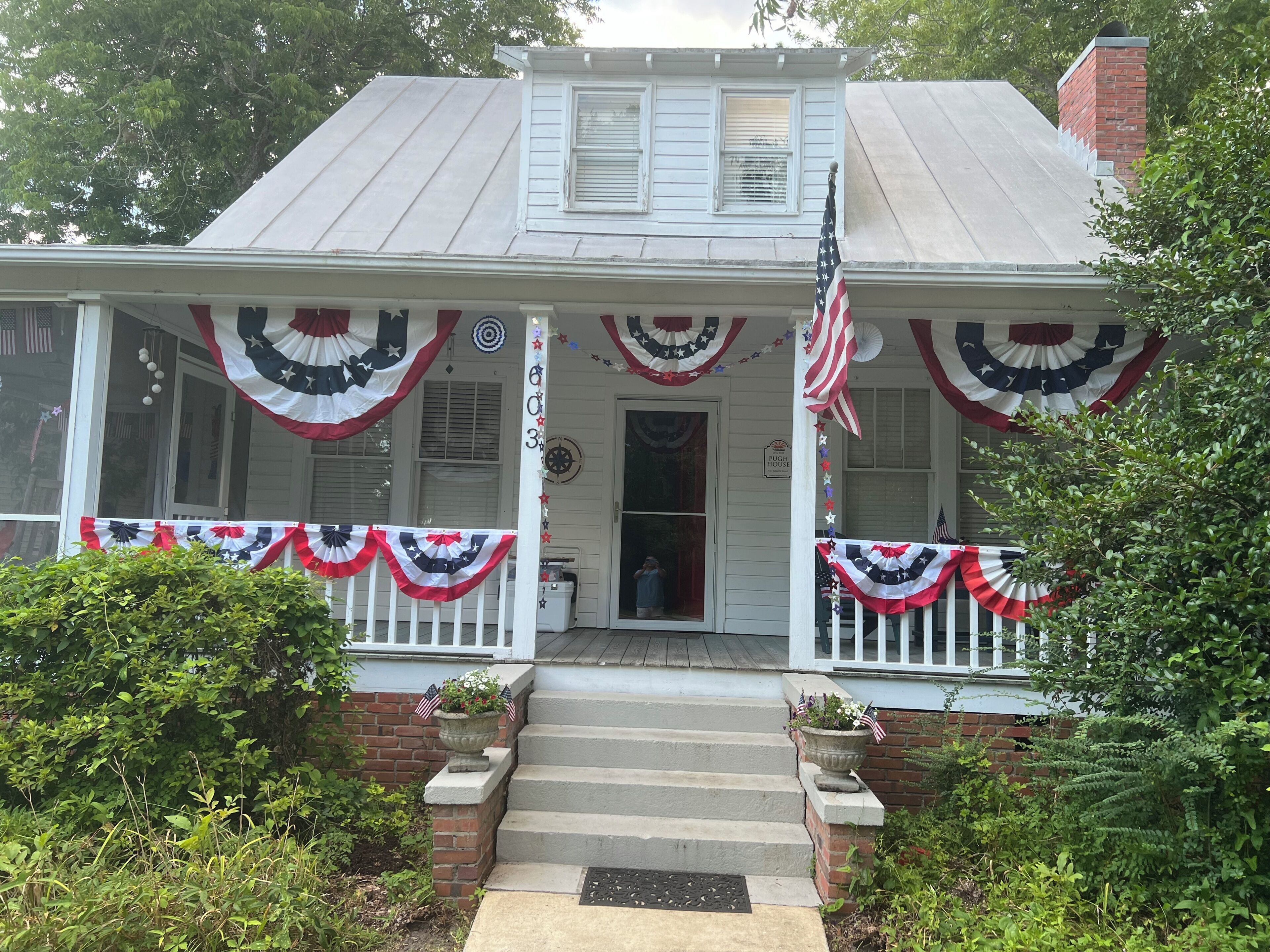 A two-story house with a porch decorated with American flags and patriotic bunting.