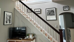A staircase with white railings and a black handrail, leading to a landing with a flat-screen TV and a small plant on a wooden console. - Experience old Oriental (Oriental)