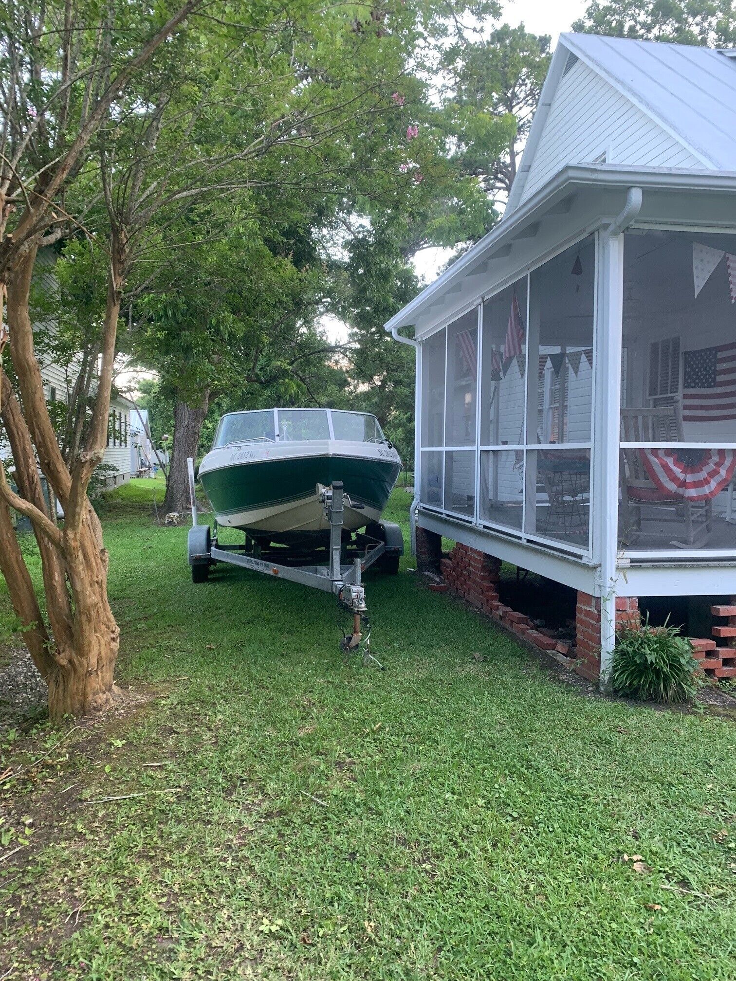 A boat on a trailer in a grassy area next to a house with a covered porch.