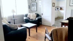 A living room with a sofa, a coffee table, and a chair. There is a door leading to a kitchen area. - Experience old Oriental (Oriental)