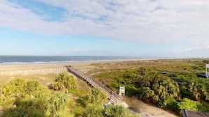 A coastal landscape with a wooden walkway leading to a beach, surrounded by greenery and a clear sky. - Oceanfront Oasis (Tybee Island)
