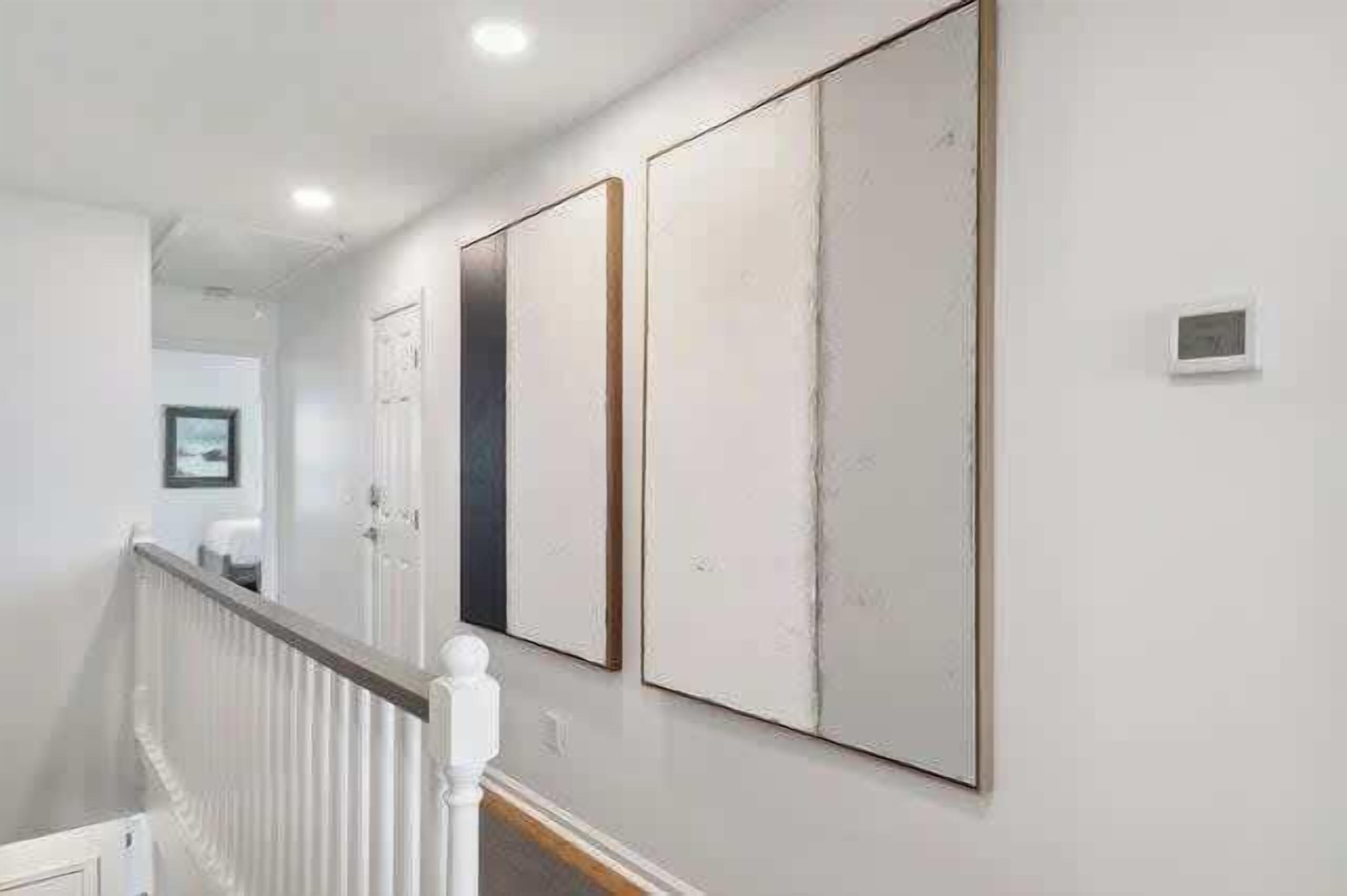 A hallway with a white railing, a door, and three large, rectangular artworks on the wall.
